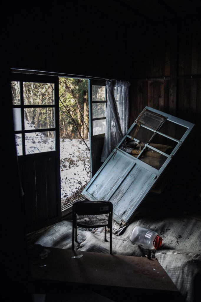 桑崎冬季分校の教室内。外れた水色の木製扉が斜めに立てかけられ、その前に小さな椅子が一脚だけ残された、静まり返った学び舎の光景。