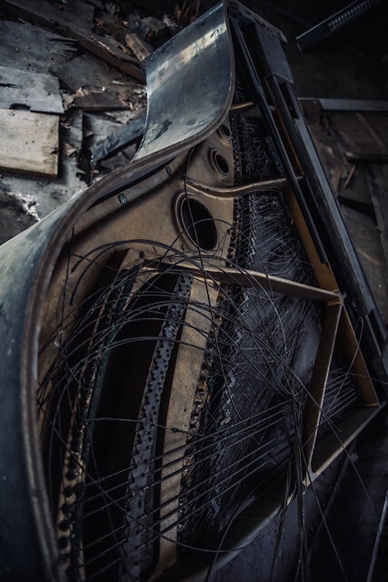 倒壊したグランドピアノの内部。張力を失ったピアノ線が乱雑に絡まり、錆びた金属フレームが露出している様子。