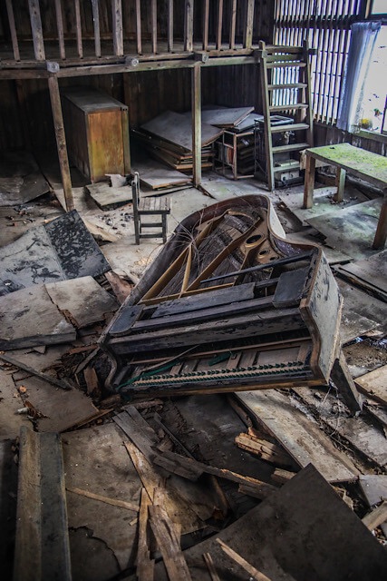 桑崎冬季分校の音楽室にて、腐朽した床が抜け、地面に沈み込んだグランドピアノ。鍵盤は失われ、周囲には剥落した天井や床板が散乱している。