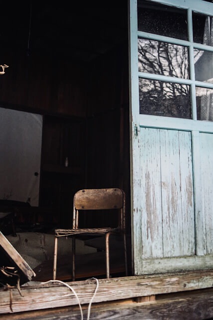 桑崎冬季分校の入り口付近に残された、座面が傷んだ木製の小さな椅子。開いた扉から差し込む光が、静まり返った教室内を照らし、人の営みの名残を感じさせる光景。