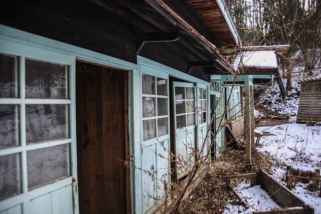 雪の中に佇む桑崎冬季分校の校舎。屋根の一部が抜け、水色の窓枠が歪むなど老朽化が進んでいる木造校舎を近くから見た様子。