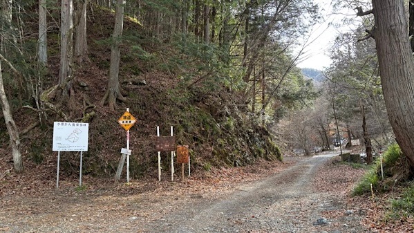 県道から分岐する林道桑崎線の入り口。左手には「水源かん養保安林」などの看板が並び、道はここから未舗装の砂利道(ダート)へと変わる山中の風景。