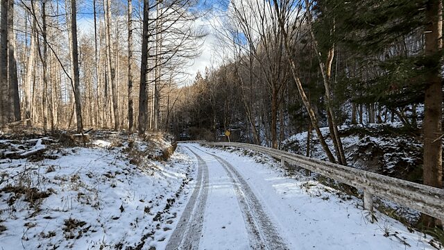 桑崎集落へと続く険しい山道。ガードレールの先は深い谷になっており、路面は一面の雪と凍りついたわだちに覆われ、周囲を冬枯れの木々に囲まれた過酷な道のり。