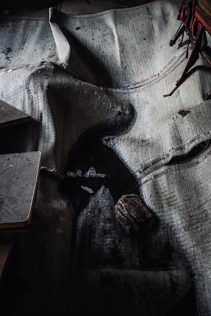 桑崎冬季分校の教室内。湿気と腐朽によって激しく波打つように変形したゴザ敷きの床。中央には雨漏りによるものか、黒く大きな染みが広がり、自然に還りつつある内部の様子。