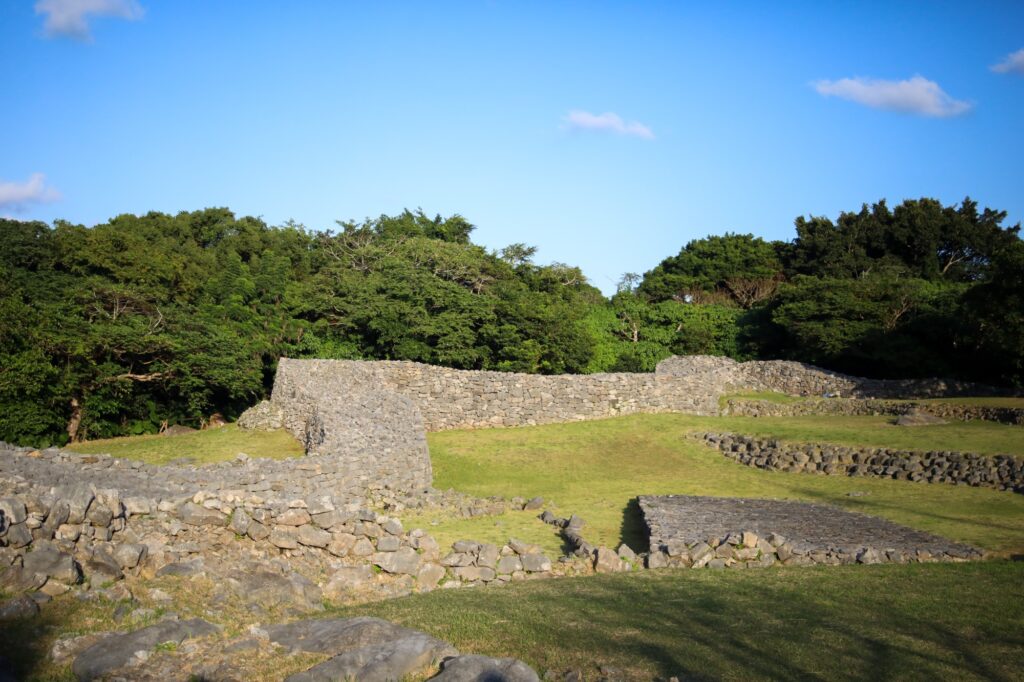 青空と緑豊かな木々を背景に、地形に合わせて緩やかな曲線を描きながら長く続く今帰仁城跡の石垣。