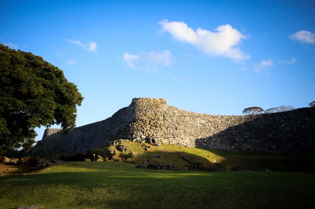 冬の深く澄んだ青い空を背景に、龍の背中のようにうねりながら続く今帰仁城跡の美しい石垣。観光客の姿はなく、静寂に包まれた世界遺産の全景。