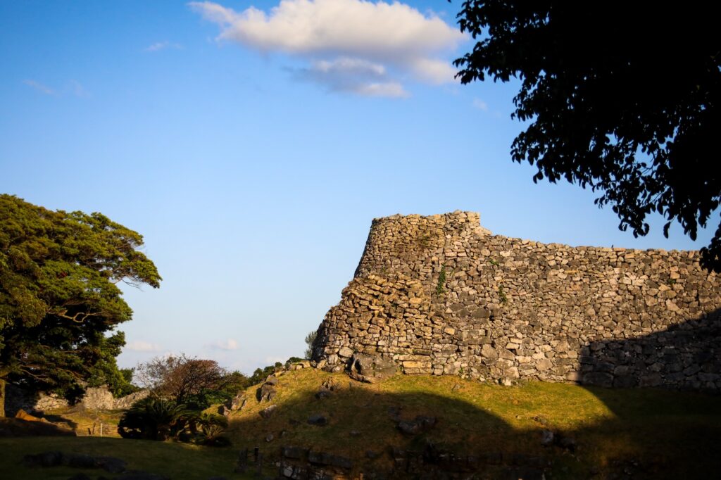 青空と豊かな緑を背景に、地形に合わせて長く、緩やかに波打つように続く今帰仁城跡の石垣。周囲に他の観光客は見当たらず、静まり返った城内の風景。