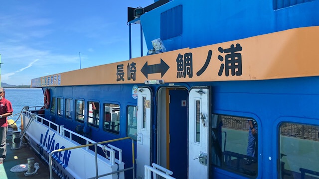 新宮港に停泊している、青い船体の相島行き連絡船。本来の航路とは異なる「長崎 ↔ 鯛ノ浦」というオレンジ色の看板が設置された代役の船の様子。