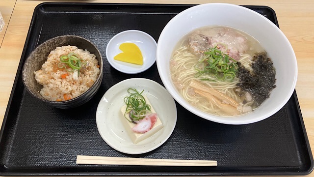 鞆の浦らーめん 鯛丸の「鯛めし定食」。透き通ったスープの鯛だしラーメン、具だくさんの鯛めし、タコが添えられた冷奴、黄色いたくあんが黒いトレイに乗った豪華なランチセット。