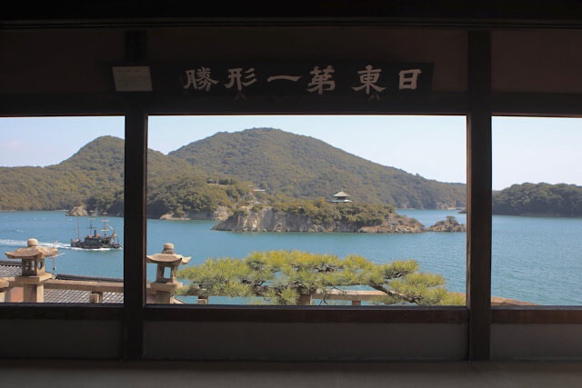 福禅寺対潮楼の室内から、柱と鴨居を額縁に見立てて眺めた瀬戸内海の風景。穏やかな海に弁天島と仙酔島が浮かび、左側には「いろは丸」を模した渡船が波を立てて走っている。鴨居の上には「日東第一形勝」と書かれた扁額が掲げられている。