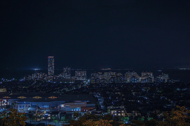 福岡の鷲尾愛宕神社から見下ろす、夜の福岡市街地と博多湾の夜景。奥にシーサイドももち地区の高層マンション群、手前に広大な住宅街の灯りが広がる。デートや告白におすすめの絶景。