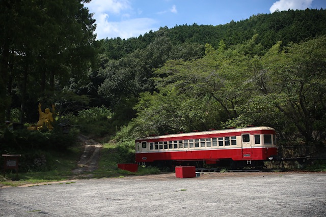 夏の青空と青々とした山林を背景に、静態保存されている片上鉄道キハ311形気動車が佇む遠景。赤とクリーム色のツートンカラーの車体が緑に映える。