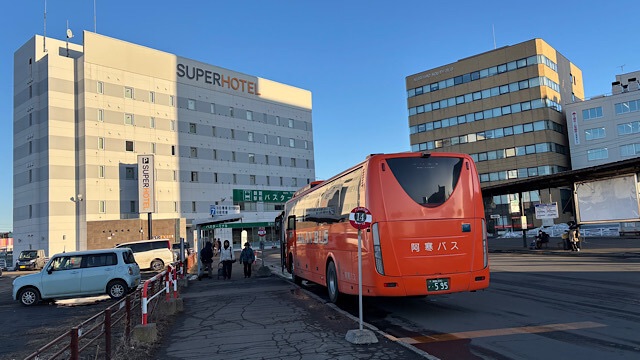 JR釧路駅横のバスターミナルに停車中のオレンジ色の阿寒バス。背景にはスーパーホテル釧路駅前が見える、冬の快晴の日の様子。