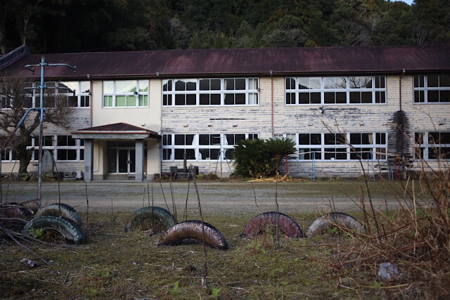 校庭の半分埋まったタイヤの遊具越しに見る、旧九鬼小学校の大きな木造校舎。剥げかけた外壁の質感が歴史の深さを物語っている。