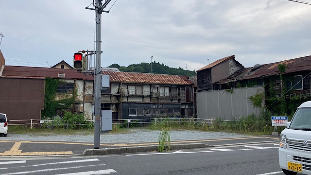 国道309号線沿いに建つ下渕マーケットの外観。古い木造とトタンが連結した長大な長屋構造の建物が並び、錆びた屋根や蔦に覆われた壁面が激しく老朽化している。手前には信号機や道路の白線が見える。