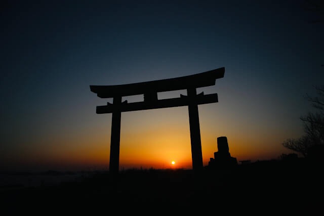 「天空の鳥居」の真ん中に夕陽が重なるシルエット。燃えるようなオレンジ色の空と水平線の絶景。