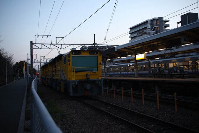 夕暮れの杉本町駅ホームの脇で、かつての阪和貨物線から転用された留置線に停車している黄色い大型の鉄道保線車両