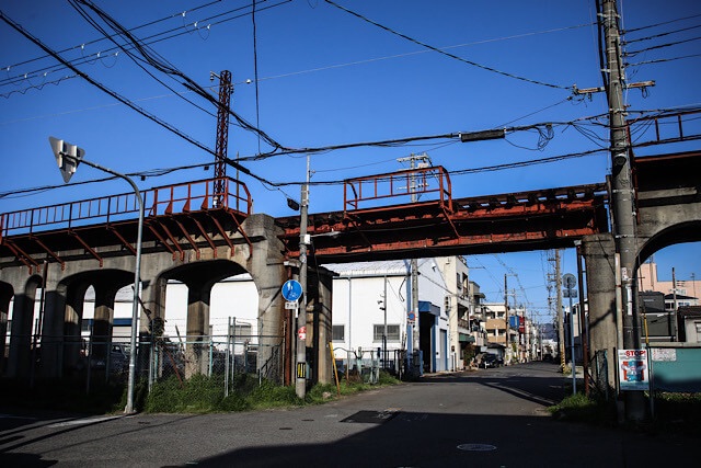 一般道路をまたぐように残されている、コンクリート高架橋と赤茶色に錆びた鉄桁(ガーター橋)。まだ橋の上には線路が残されているようだ。