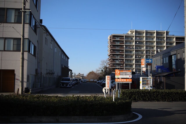 手前のビルや奥のマンションに挟まれるように、細長く直線的に舗装されて駐車場の一部となった阪和貨物線の跡地