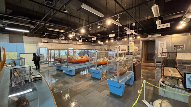 稚内市青少年科学館の展示室。中央に置かれた南極観測船の精密模型ケースや、手前に置かれた犬ぞりの展示など、昭和レトロでノスタルジックな雰囲気が広がる館内風景。