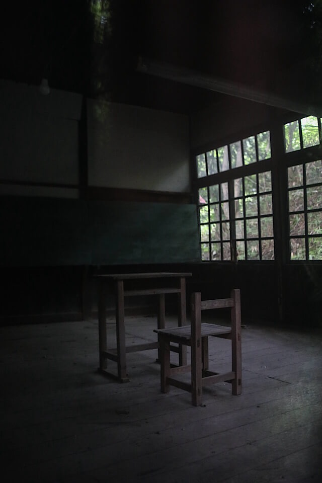 「旧入山分校」の教室。黒板と、窓から差し込む光の中にぽつんと置かれた木製の机と椅子の様子。