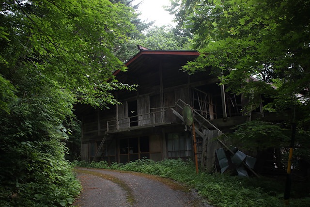 豊かな緑に囲まれた長野県松本市の廃宿場町「入山宿」の古い木造家屋と道路の様子。