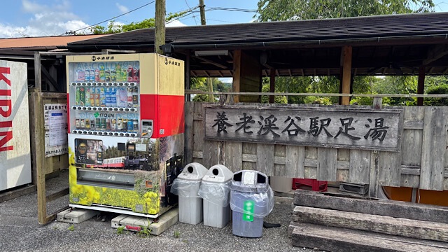 養老渓谷駅の構内にある「養老渓谷駅足湯」の木製看板と、小湊鐵道デザインのラッピング自販機。