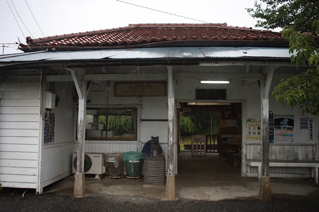 里見駅の赤瓦と白い板張りの木造駅舎外観と、改札前で出迎える犬の石像。