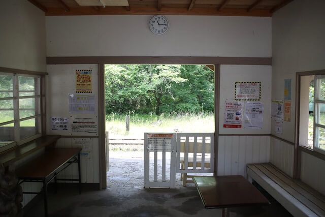 月崎駅の待合室内観。白い木製改札口の向こうに初夏の眩しい緑が広がる無人駅の風景。