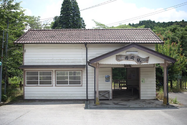 月崎駅の白い下見板張りの木造駅舎外観と、木彫りの駅名看板。