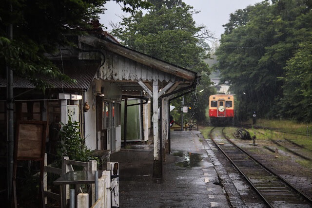 雨に濡れる小湊鐵道・里見駅の木造駅舎、ホームと去り行く列車。
